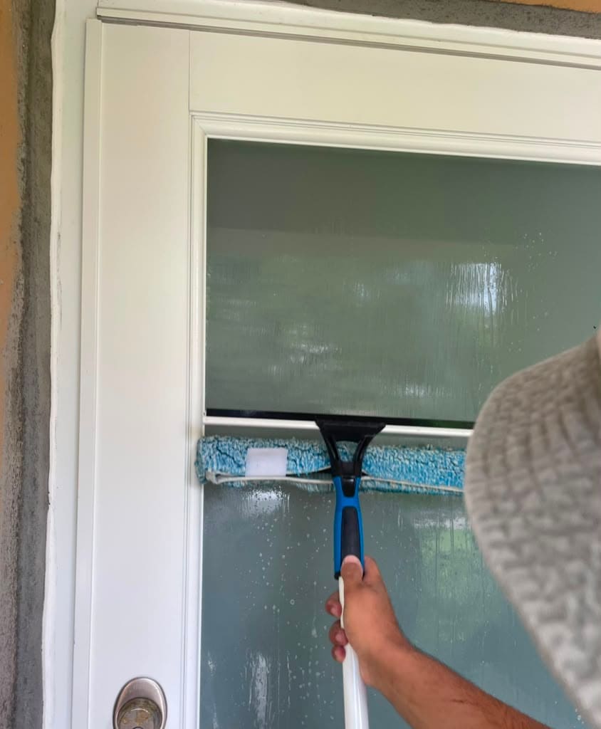 Crystal Cleaning 305 technician using a squeegee to hand-clean a glass door in Miami